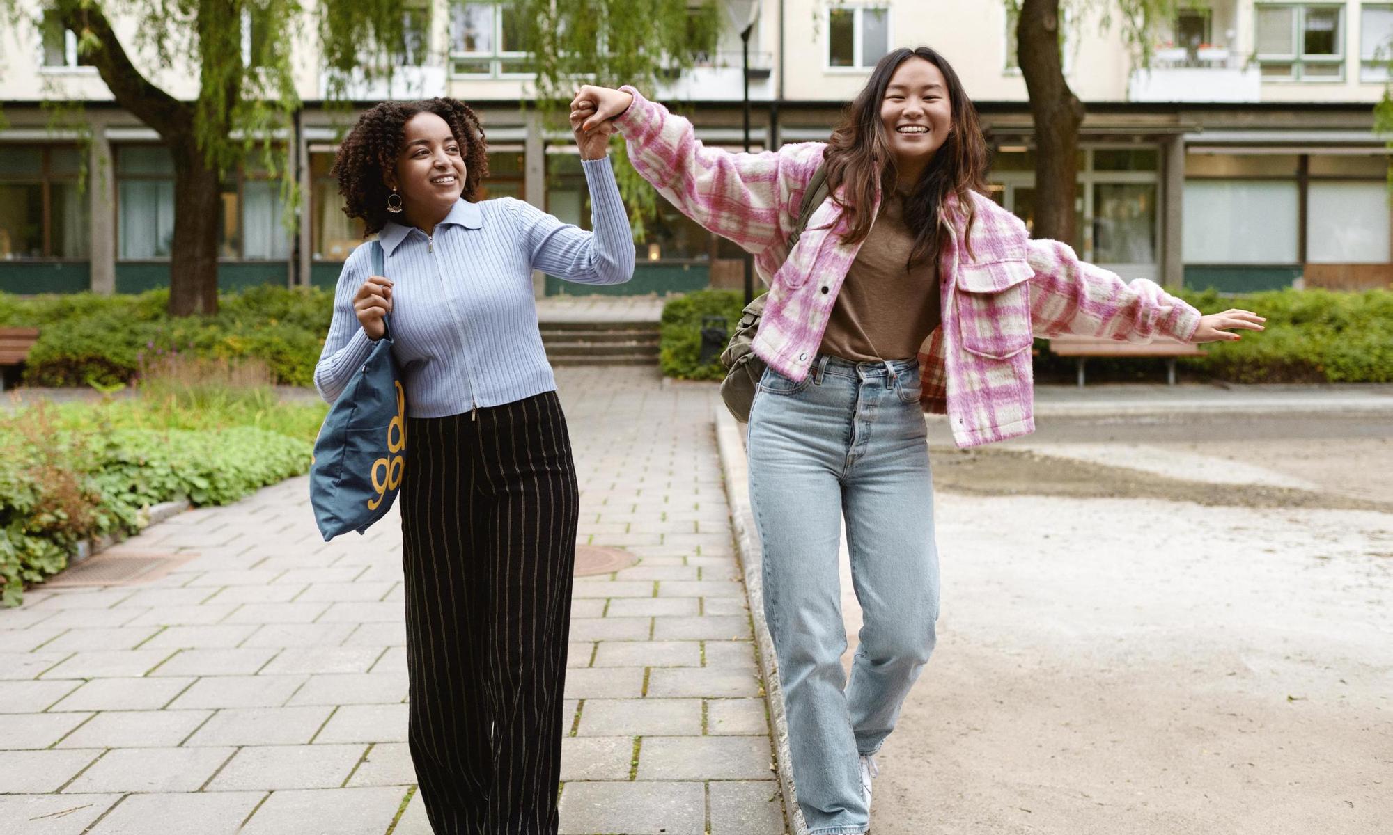 Two young women in a balancing act on the edge of a pavement