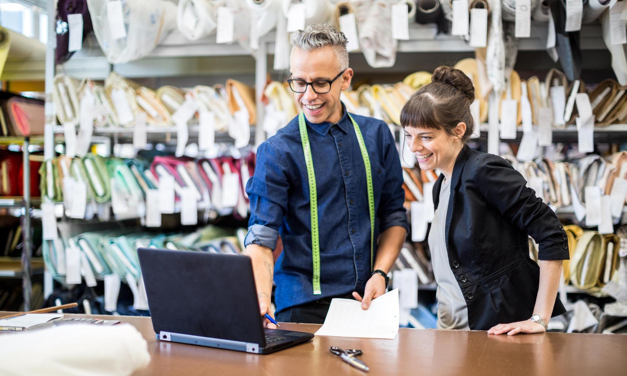 Two coworkers standing at workbench looking at laptop