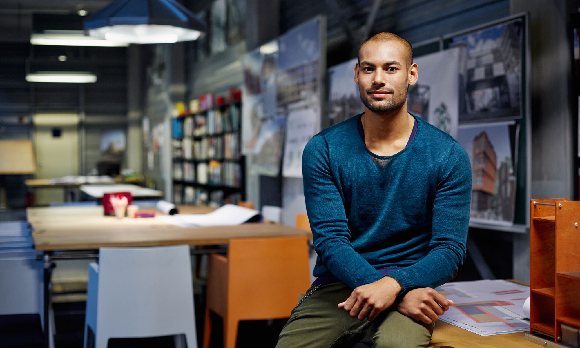 Man med blå tröja sitter på et skrivbord på ett arkitekt kontor