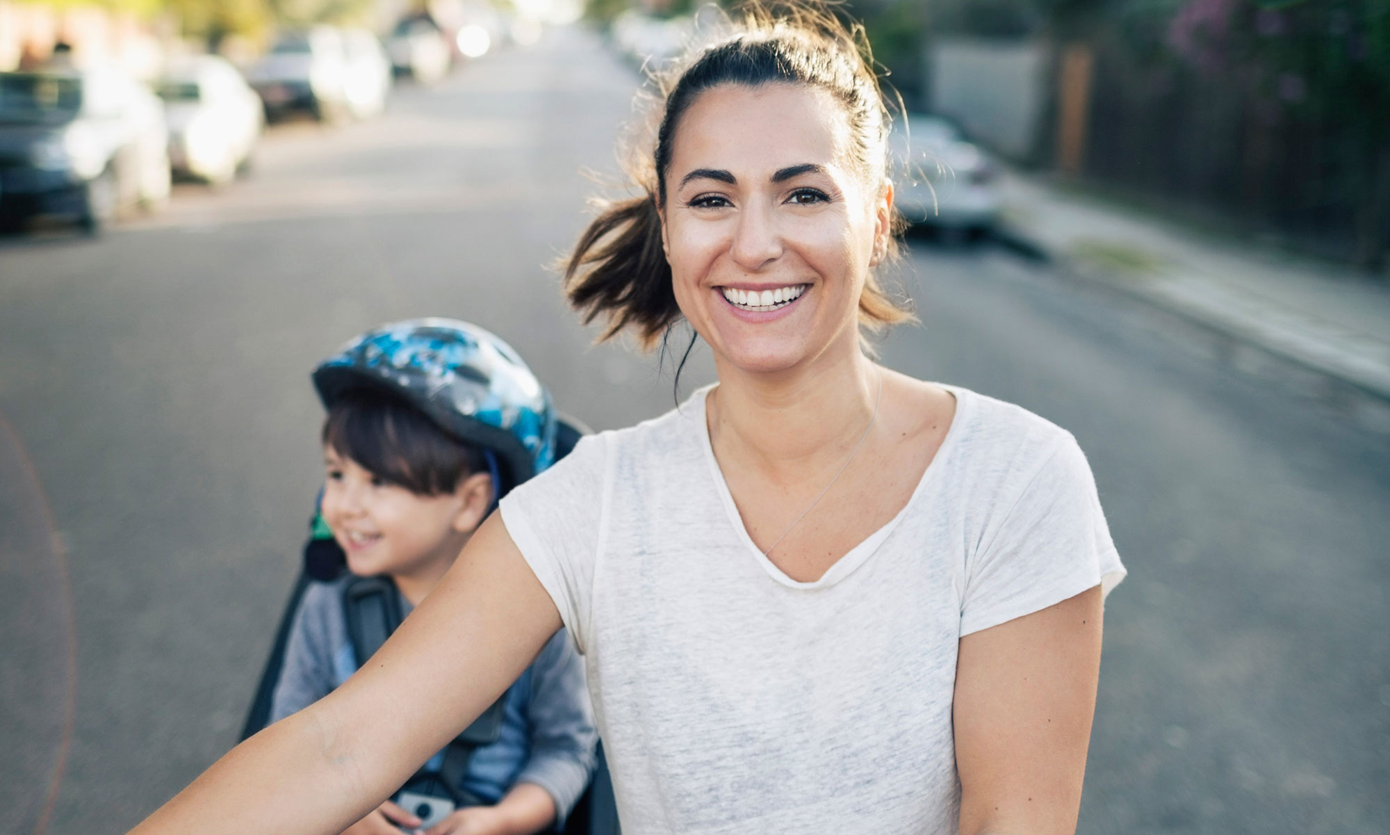 Leende kvinna leder en cykel med ett barn i cykelstol på en härlig sommardag