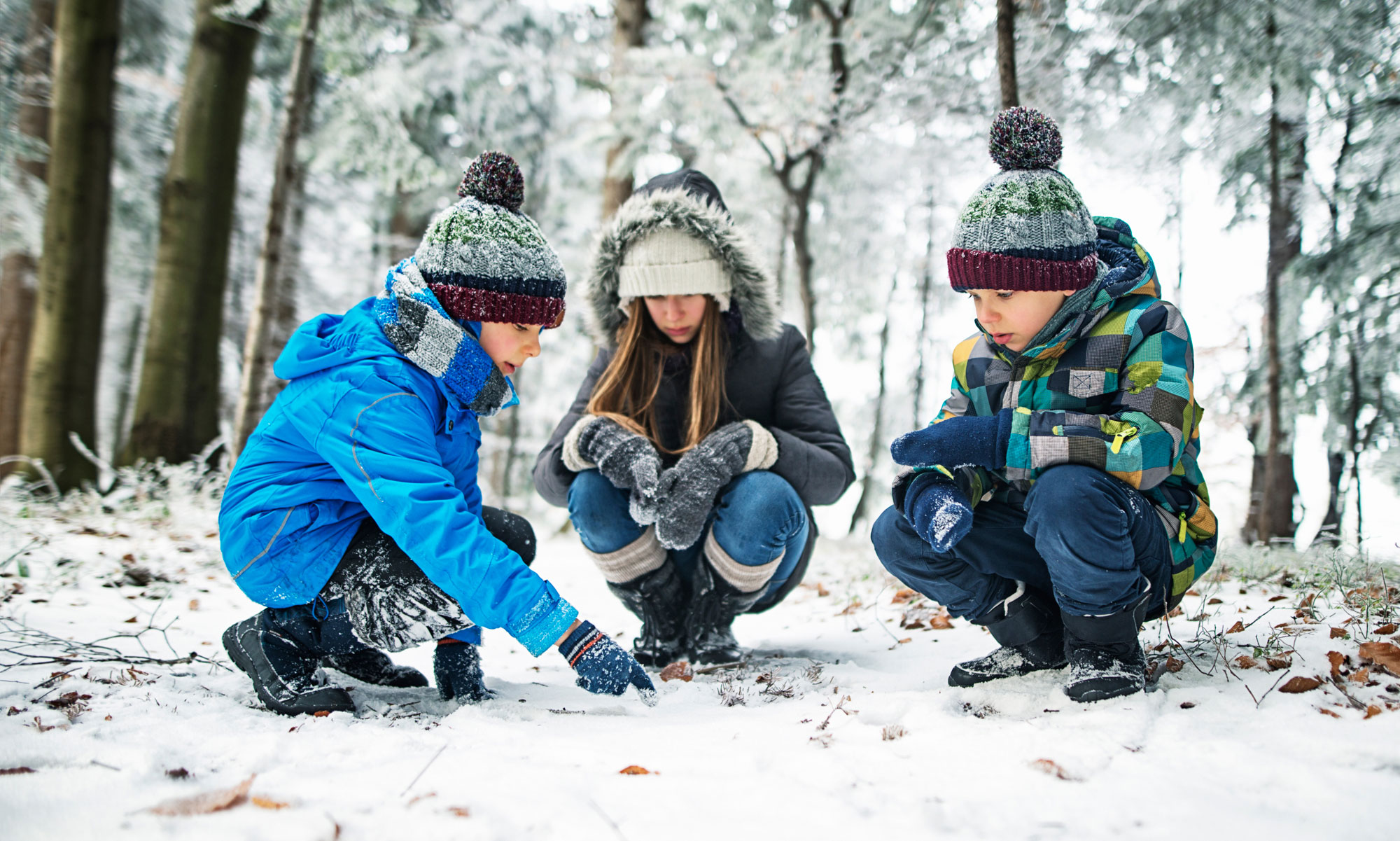 Tre barn sitter på huk i en snöig skog