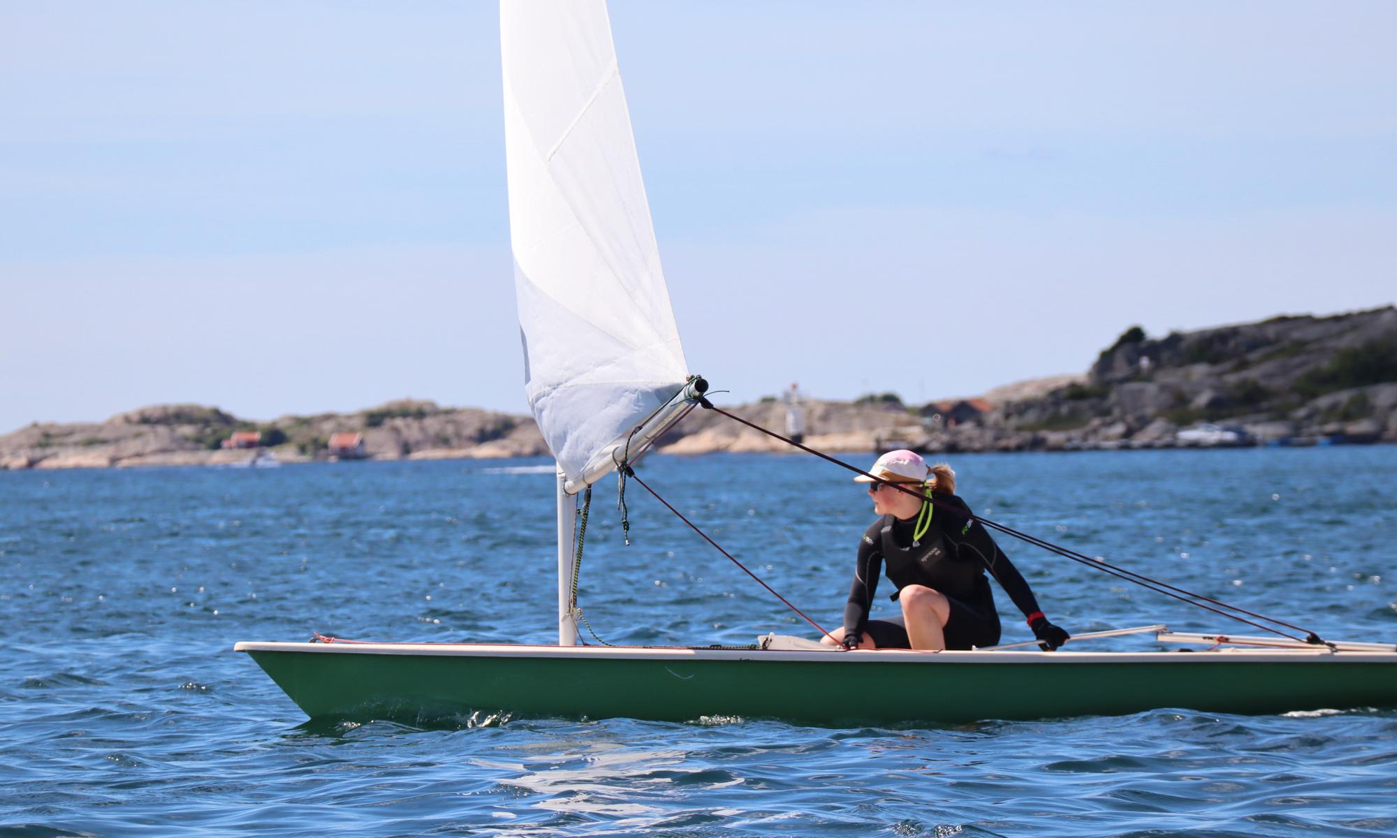 En tjej sitter och seglar i en segelbåt på havet