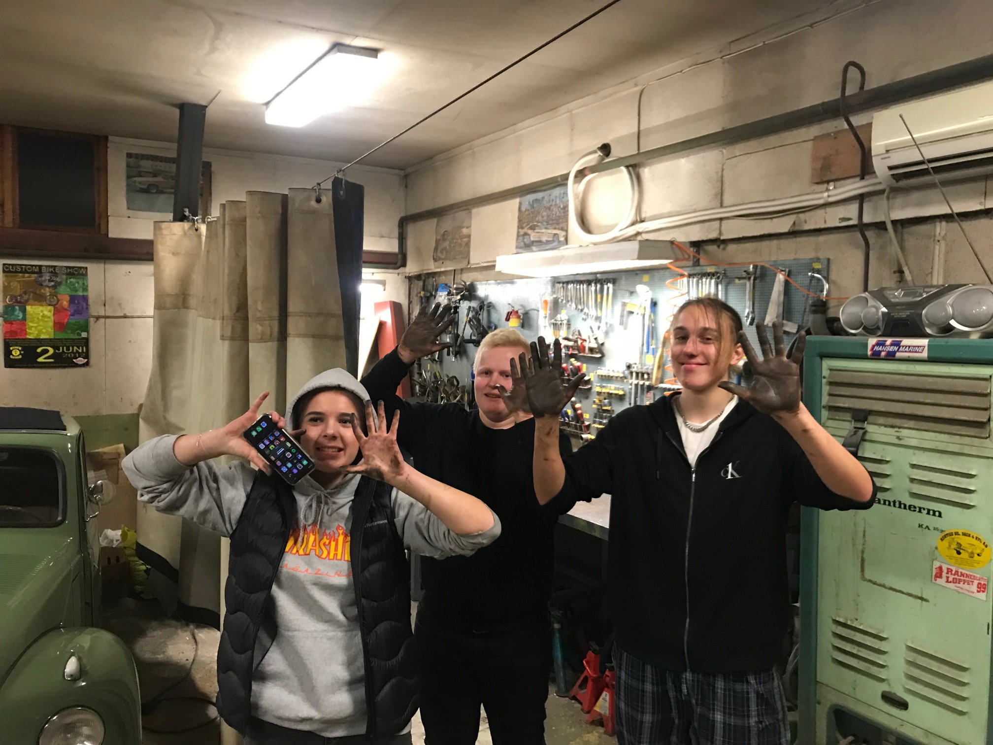 Tre killar står i ett garage och visar upp sina smutsiga händer