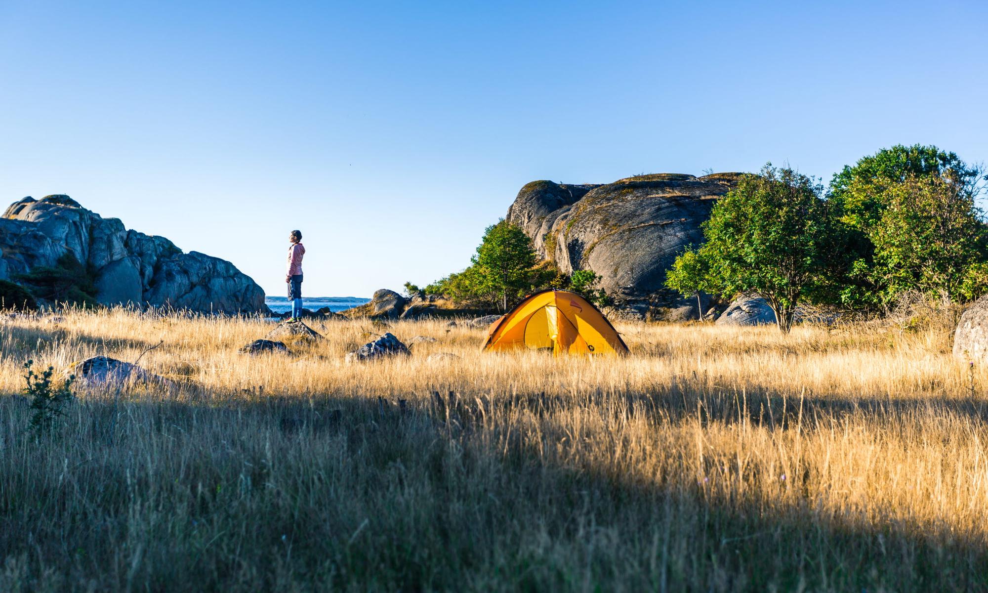 En person tältar på en åker vid havet